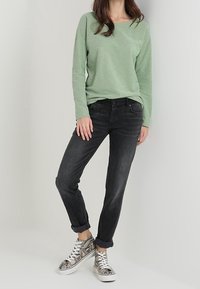 Camicia a maniche lunghe verde chiaro, jeans neri e sneakers argento con stampa serpente e suola bianca. Cuffs arrotolati sui jeans, camicia con texture.