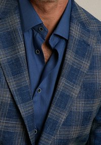 Blå rutigt blazer i texturerat tyg med kontrasterande bruna linjer; lager på ett enfärgat blått sk Fjällen med ett fint rutmönster och svarta knappar.