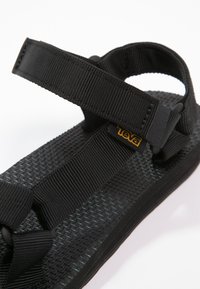 Sandalo nero con suola in gomma testurizzata, cinturini in tessuto e un'accenno al logo. I cinturini presentano un meccanismo di chiusura sicuro.