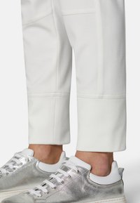 Weiße, verjüngte Hose aus strukturiertem Stoff, mit einer Nahtdetail am Saum. Kombiniert mit metallisch silbernen Sneakers mit weißen Akzenten.