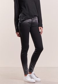 Czarne dżinsy z efektem wyblaknięcia, dopasowane w slim fit, z pięcioma kieszeniami. W połączeniu z czarną bluzką z długim rękawem i białymi trampkami.