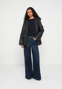 Czarna, wodoodporna kurtka z kapturem, o smukłym kroju i przednimi kieszeniami. Połączona z szerokimi, ciemnoniebieskimi spodniami dżinsowymi.