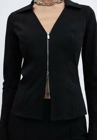 Black fitted blouse with long sleeves, notched collar, and a front zipper closure. Smooth fabric with a structured design and minimal detailing.