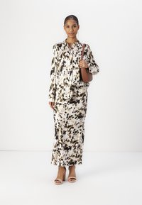 Completo composto da blusa a maniche lunghe e gonna color avorio con motivi astratti in nero e marrone; abbinato a una borsa a spalla marrone e tacchi rosa.