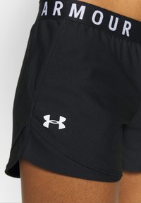 Pantalones cortos deportivos negros con un logo blanco de "Under Armour" en el dobladillo. Cuenta con una cinturilla flexible con letras en contraste. Textura suave.