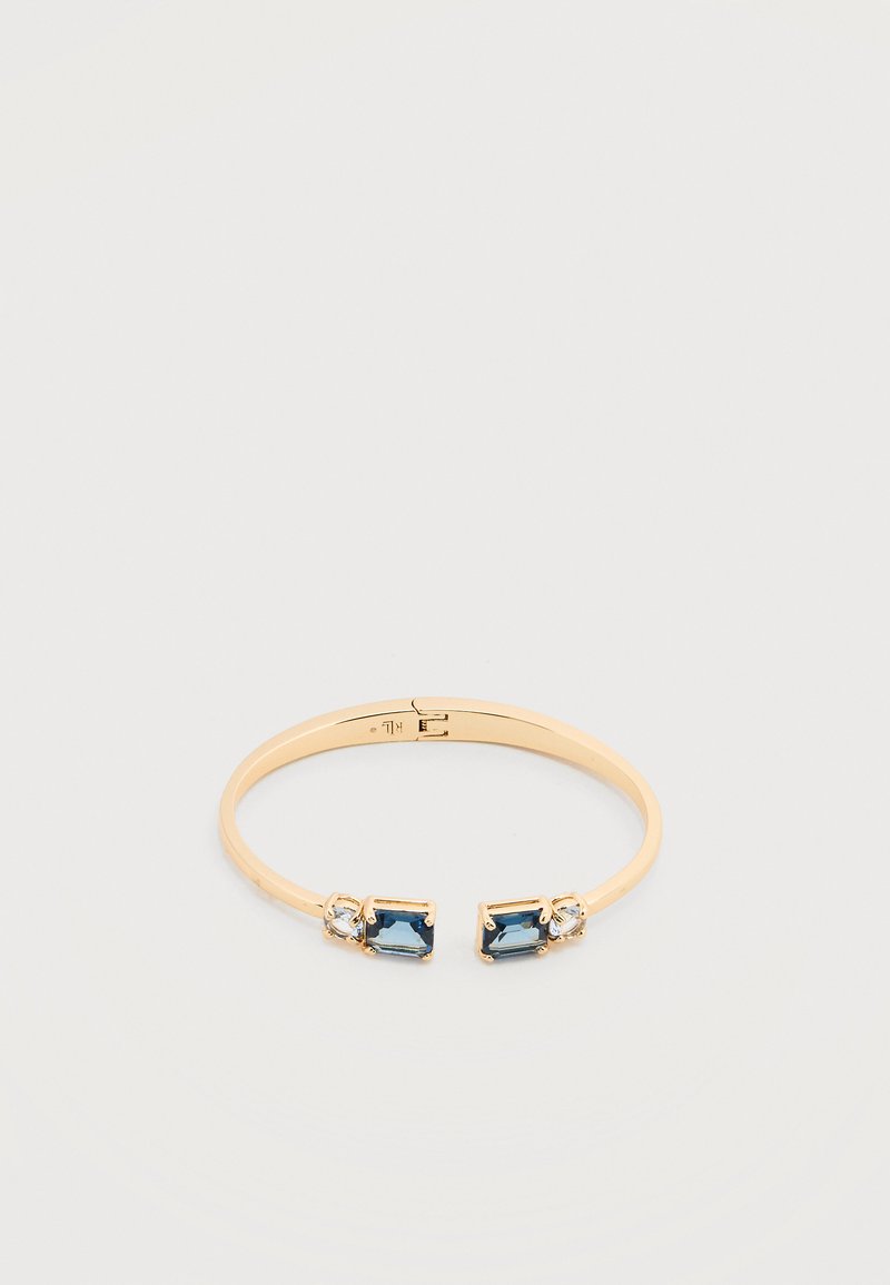 Ανοιχτό βραχιόλι σε χρυσό τόνο με ορθογώνιους μπλε λίθους και μικρούς διαυγείς στρογγυλούς κρυστάλλους σε κάθε άκρο πάνω σε φωτεινό φόντο.