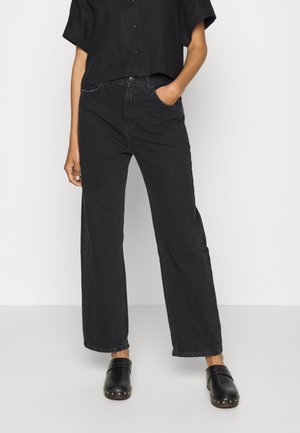 Jeans amplios negros de mezclilla, con una cintura alta, bolsillos delanteros y un ligero desgaste. Combinados con zuecos negros con acentos metálicos.