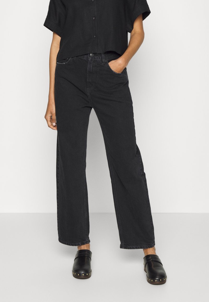 Jean large noir en denim, avec une taille haute, des poches avant et un léger délavage. Assortis à des sabots noirs avec des accessoires en métal.