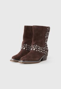 Botine din piele suede maro închis, cu toc mediu, capace metalice pe vârfuri și aplicate diverse bibelouri mari și mici pe părțile laterale și marginile superioare.