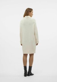 Abito maglione oversize color crema con collo alto, maniche a coste e orlo dritto, indossato con stivali neri fino al ginocchio.