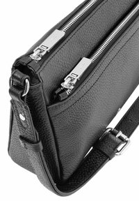 Czarna skórzana torebka z dwoma zamykanymi na zamek przegrodami, teksturowaną powierzchnią i regulowanym paskiem z metalowymi detalami.
