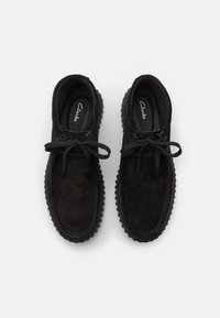 Svarta mockaskor med runda snören, rund tå, texturerad gummisula och stickade detaljer längs kanterna.