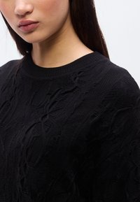 Μαύρο πλεκτό πουλόβερ με υφασμένους μοτίβους και ριμπ λαιμόκοψη. Το ύφασμα φαίνεται μαλακό με ελαφρώς χαλαρή  εφαρμογή.