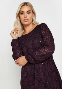 Vestido de encaje de manga larga de color púrpura profundo con patrones florales y lentejuelas, con un escote redondo y mangas ligeramente abullonadas.