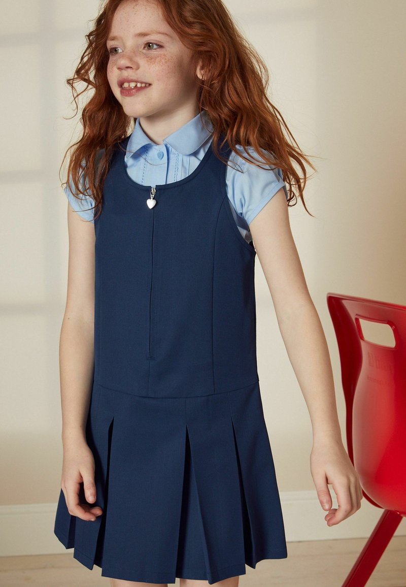 Robe bleu marine avec des plis, présentant un col rond et une fermeture éclair en forme de cœur argenté. Chemise à col bleu clair en dessous.