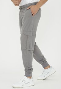 Grå joggers med elastisk midja, cargoficka, ribbade manschetter och mjukt, texturerat tyg. Matchas med vita sneakers för kontrast.