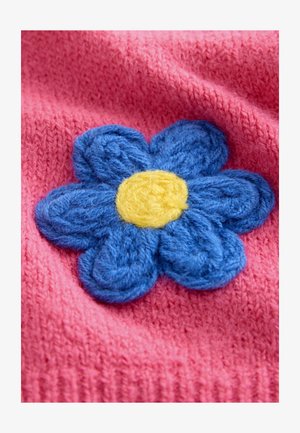 Rozā adīts audums ar zilu, fakturētu zieda aplikāciju, kuras centrā ir dzeltens punkts. Ziedam ir 3D efekts ar kārtotām ziedlapiņām.