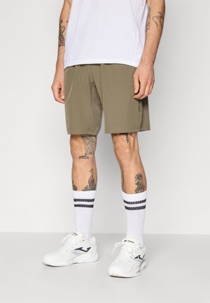 Khaki-Shorts aus leichtem Stoff verfügen über Seiten Taschen und werden mit weißen Sportschuhen und gestreiften weißen Socken kombiniert.