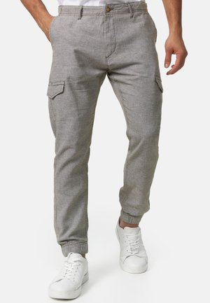 Graue, taillierte Cargo-Hosen mit elastischen Bündchen, ausgestattet mit Seitentaschen und einem Knopfverschluss, aus strukturiertem Stoff. Kombiniert mit weißen Turnschuhen.