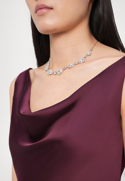 Ασημένιο κολιέ με ανθικά στοιχεία, που διαθέτει πολλούς διαυγείς πολύτιμους λίθους, φορεμένο με βαθύ μπορντό σατινέ τοπ με λαιμόκοψη καζούαλ.