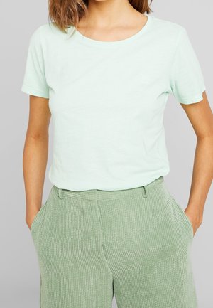 Camiseta de algodón verde claro con escote redondo y mangas cortas, combinada con pantalones verdes texturizados que presentan patrones de canalé vertical.