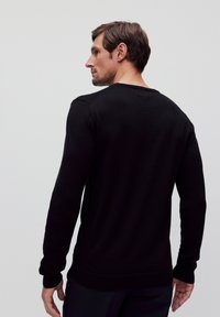 Zwarte longsleeve trui met een ronde hals, geribde manchetten en zoom. Gemaakt van gladde stof, heeft een getailleerd ontwerp en strakke lijnen.