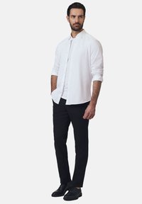 Biała, długa koszula z długim rękawem, wykonana z lekkiego materiału, z zapięciem na guziki. Połączona z czarnymi spodniami o slim-fit i czarnymi butami wizytowymi.