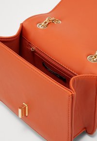 Borsa a mano in pelle arancione con texture liscia, dotata di dettaglio in catena dorata e tasca interna con zip. Chiusura metallica di forma rettangolare.