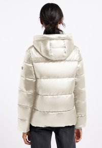 Puchowa kurtka z kapturem w kolorze off-white, z pikowanymi sekcjach i gładką, błyszczącą powierzchnią. Posiada mankiety oraz naszywkę z logo na rękawie.
