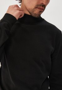 Juodas golfas su prigludusia forma ir įtempta apykakle, turintis lygų paviršių ir ilgomis rankovėmis.