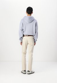 Haut à capuche bleu clair avec capuche, coupe ample, associé à un pantalon couleur crème. Les chaussures décontractées présentent des accents noirs et une semelle robuste.