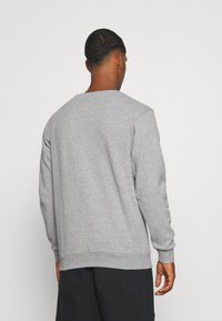 Sweatshirt gris à manches longues, col rond et poignets côtelés. Fabriqué en tissu doux et texturé. Design simple sans motifs visibles.