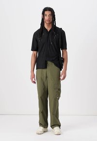 Zwarte short-sleeve button-up shirt met een ontspannen pasvorm; gecombineerd met losse olijfgroene cargobroek met zijzakken en een logo-patch.