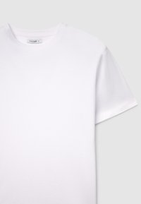 Maglietta bianca in cotone con scollo rotondo e maniche corte. Texture liscia, con un design pulito e dettagli minimi. Etichetta della taglia visibile.