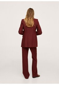 Costume sur mesure bordeaux composé d'un long blazer et d'un pantalon à jambes larges, fabriqué en tissu texturé, avec une coupe structurée et un design minimaliste.