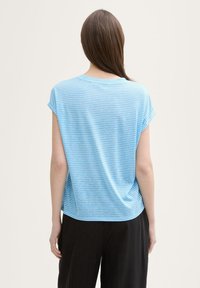 Tricou cu dungi albastre deschise, cu mâneci scurte, croială lejeră, textură moale și gât rotund, purtat cu pantaloni negri largi.
