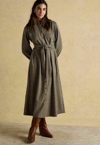 Pārbaudīta garo piedurkņu kleita zaļā, sarkanā un brūnā nokrāsā, ar sasietu jostu, pogu priekšpusi un plūstošu svārku. Brūnas ar papēžiem botas.