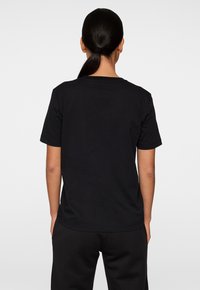 Musta lyhythihainen T-paita, joka on valmistettu pehmeästä puuvillasta. Paitassa on pyöreä kaula-aukko ja rento väljyys. Takapuolella on yksinkertainen malli ilman grafiikoita.