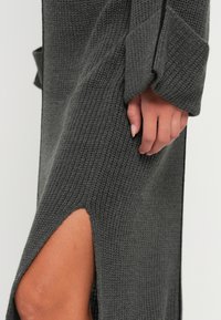 Knit long-sleeve dress in dark gray with a textured pattern and side slit. Features a relaxed fit with a rounded neckline and dropped shoulders.