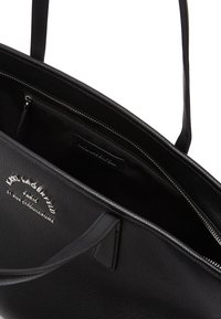 Black leather tote bag with textured surface, dual handles, and a zipped inner compartment. Silver logo detailing on the front.