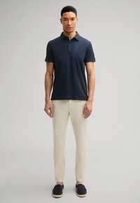 Polo de marino con cuello, que presenta mangas cortas y un logo sutil. Combinado con pantalones de color crema y zapatos de charol marinos.