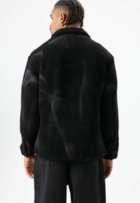 Zwarte, zachte, getextureerde jas met kraag. Voorzien van openingen aan de manchetten en een patch op de bovenrug. Casual stijl.