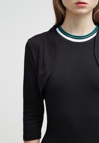 Svart långärmad topp med en texturerad, figurnära kropp och lager-på-lager framsidan. Har en flerfärgad ribbad halsringning. Enkel och modern design.