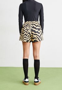 Svart långärmad topp tillsammans med shorts med ett mönster av gula och svarta zigzaggor, svarta knähöga strumpor och vita sneakers med gummisoles.