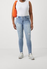 Ljusblå denim skinny jeans med slitningar, parat med en vit ärmlös topp och en orange vadderad väska.