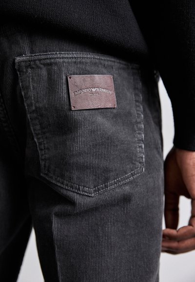 Gray corduroy pants with a textured surface, featuring a leather brand patch on the back pocket and a regular fit cut.