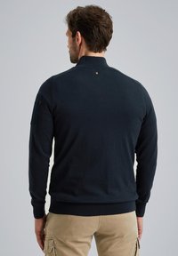 Navy blue sweatshirt with a partial zip collar, ribbed cuffs, and hem. Features a side pocket and a small logo on the back. Soft fabric texture.