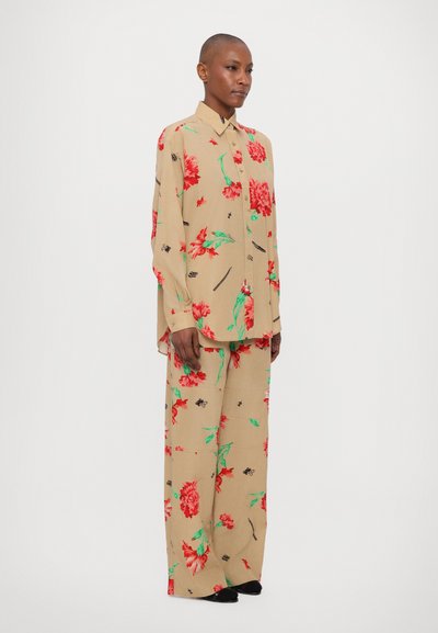 Conjunto de camisa y pantalones beige con flores rojas y hojas verdes en una tela ligera. Corte relajado con cierre de botones y mangas largas.