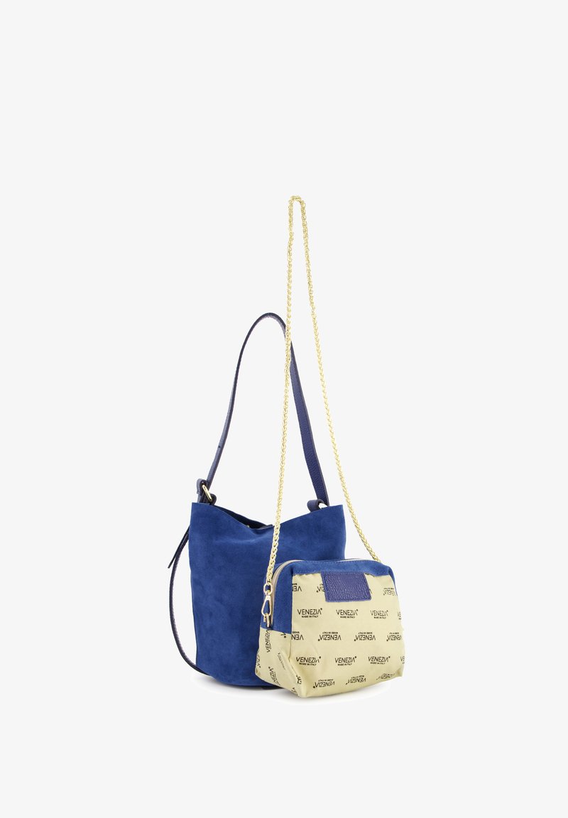 Blauwe suède schoudertas met een contrasterende crème pouch met geprinte tekst. Gouden kettinghengsel met een blauwe leren accentrits.
