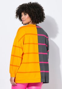 Camicia a maniche lunghe oversize colorata, caratterizzata da sezioni arancioni e grigie audaci, grandi strisce rosa, colletto arrotondato e texture morbida.